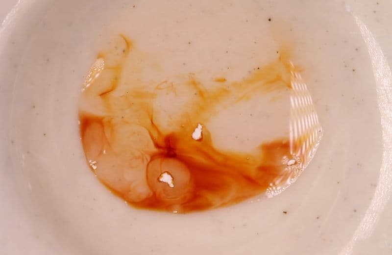 A multi-well ceramic plate showing various color reactions from reagent testing of substances.
